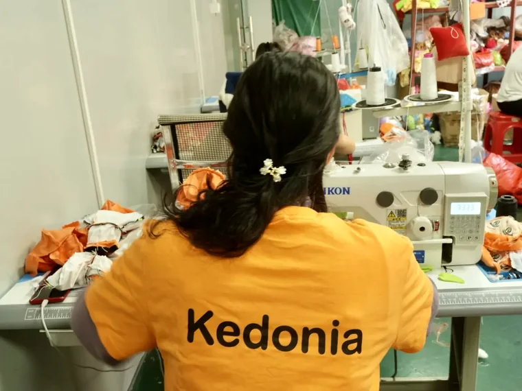 Sewing operator working with unstuffed plush shells and fabric panels at a sewing machine