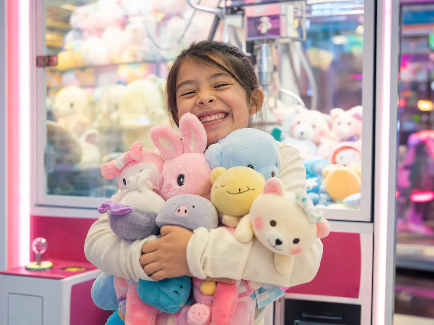 Happy child hugging a large armful of plush prizes won at a claw machine arcade