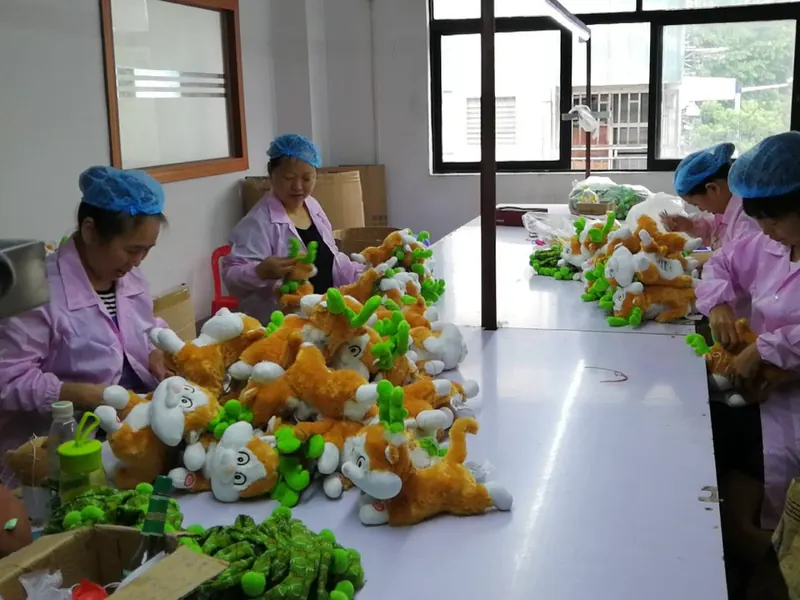 Plush sample finishing and handwork at a factory table during custom plush cost review