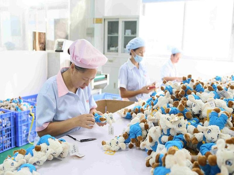 Workers inspecting finished plush toys on a factory table