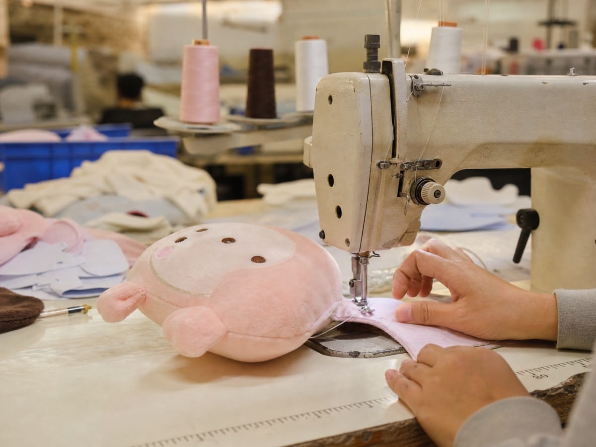 Industrial sewing machine stitching a custom plush toy inside a plush manufacturing workshop